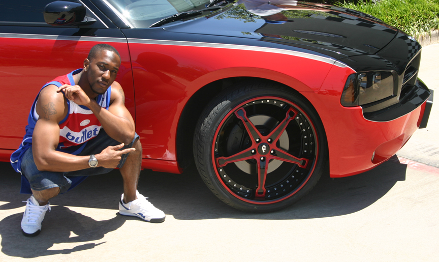  infront of his 22″ Forgiato Martellato wheels on his Dodge Charger SRT8.