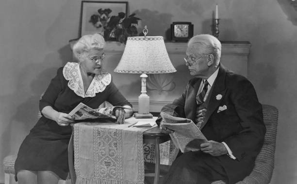 An old man reads a newspaper as wife looks through a magazine 1940's Old Photo An old man reads a newspaper as wife looks through a magazine 1940's Old Photo